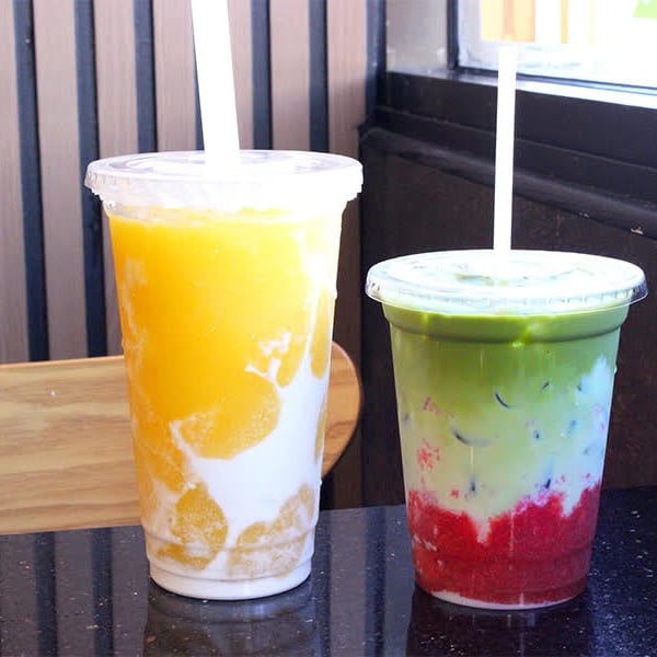 Two colorful layered drinks, one yellow and white, the other green, white, and red, on a dark counter.