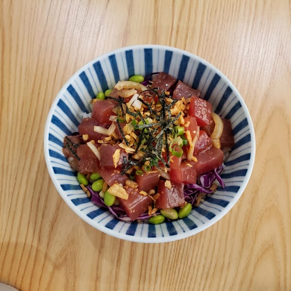 A colorful poke bowl with tuna, edamame, red cabbage, and crispy toppings in a striped bowl.