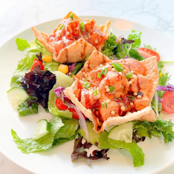 Two crispy wonton cups filled with salmon poke, drizzled with sauce, on a fresh green salad.