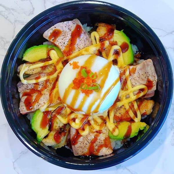 A poke bowl with seared tuna, avocado, a poached egg, and various sauces.