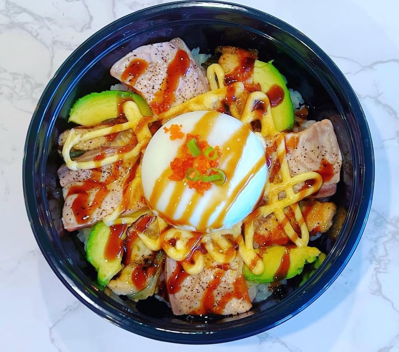 A poke bowl with seared tuna, avocado, a poached egg, and various sauces.